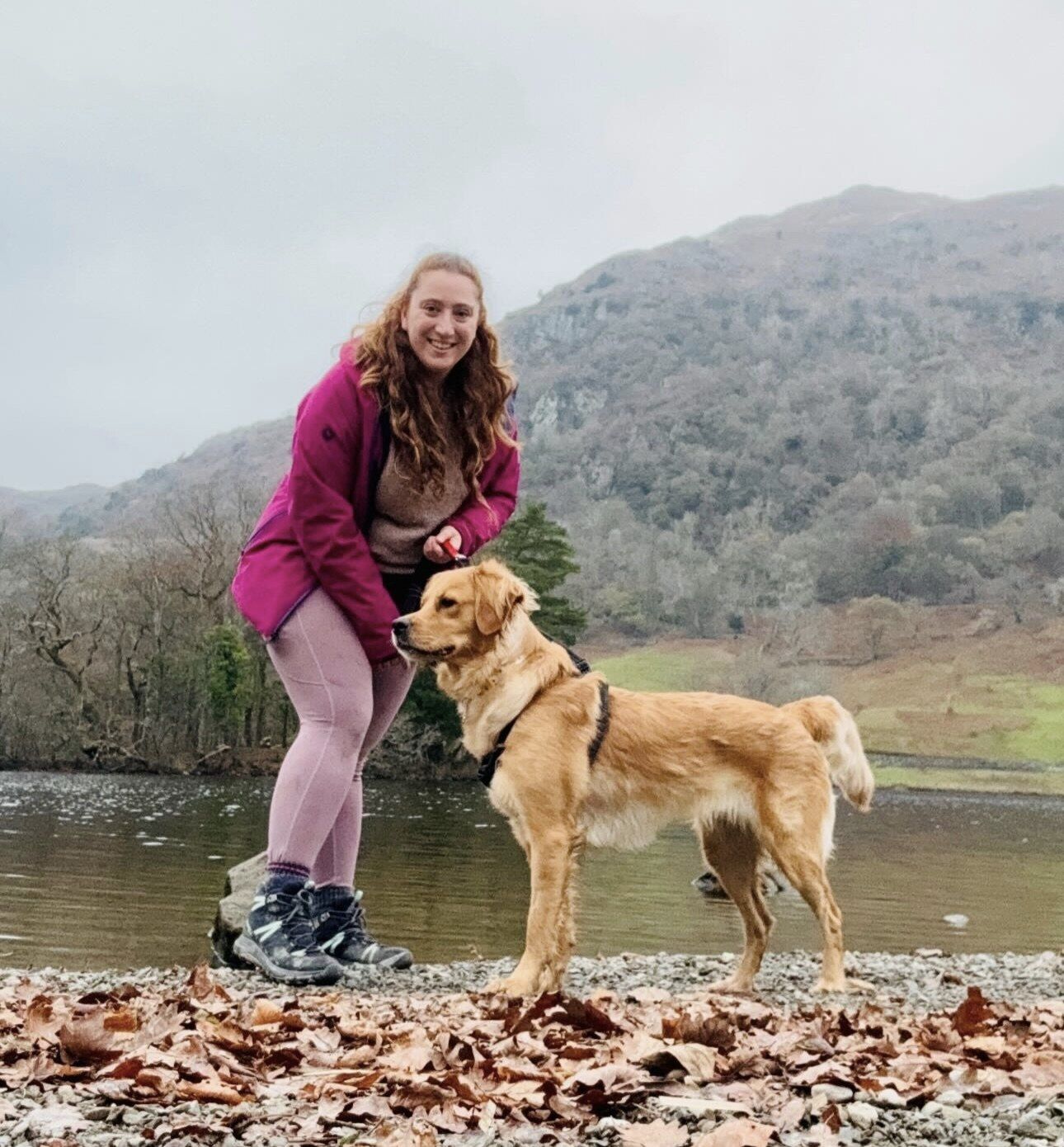Tamara beside a lake with Skye, her golden retriever, standing on fallen leaves