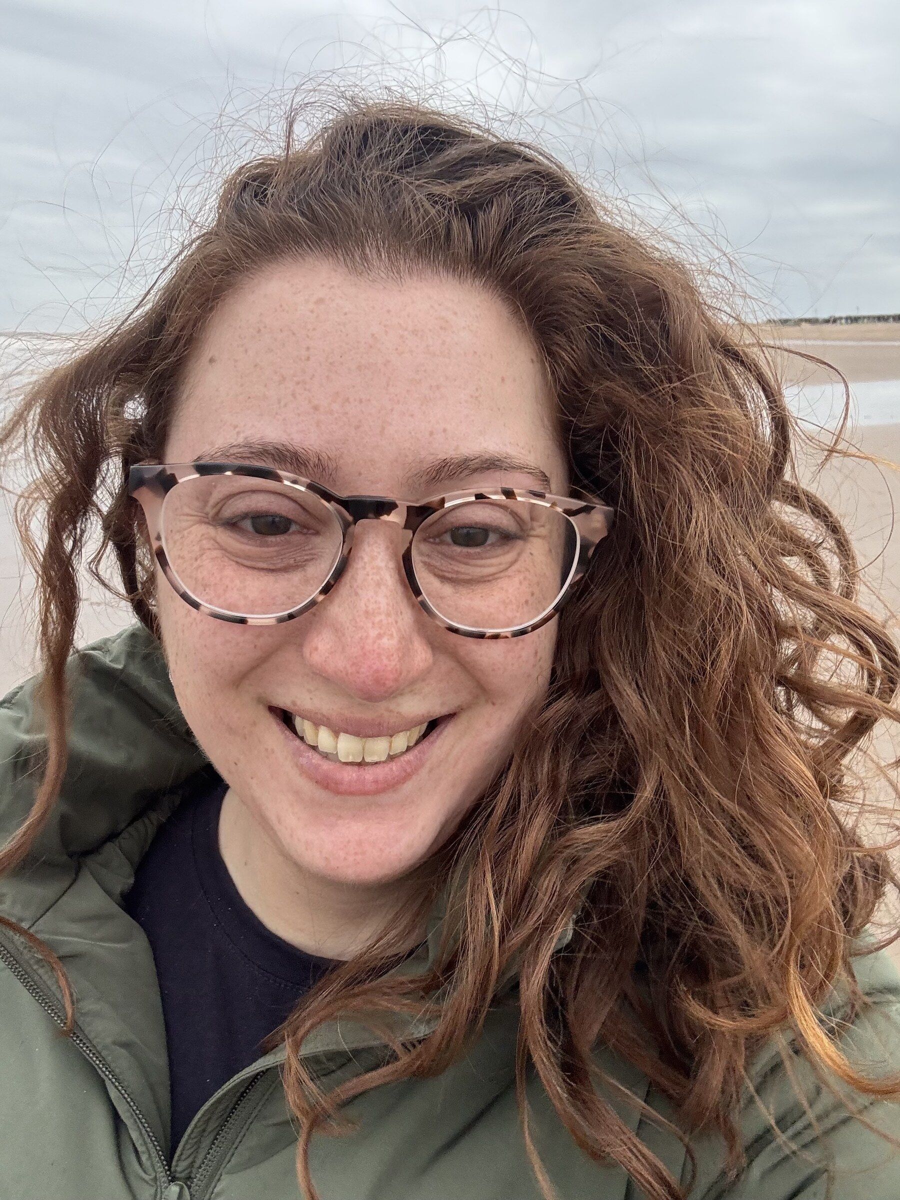 Tamara outdoors on a windy beach, hair across her face, looking at the camera